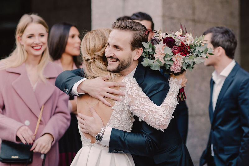 A bride with flowers in her hand hugging a guest