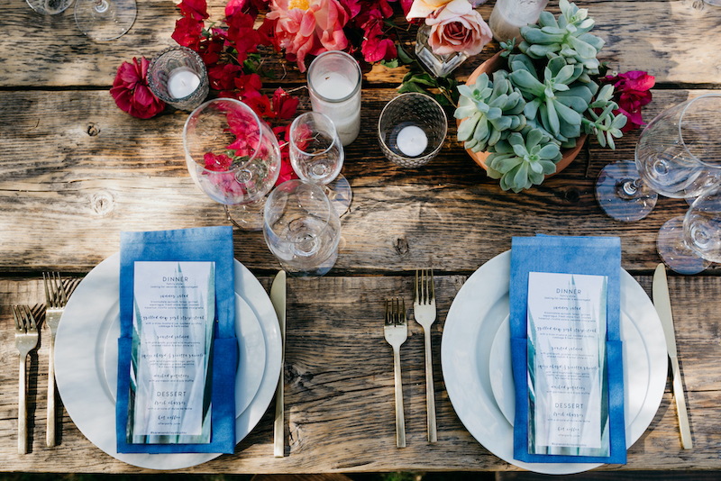 A wooden table set up for a wedding dinner with plates and glasses